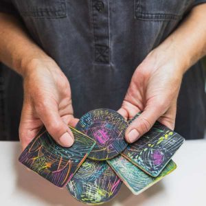 The artist holding 5 samples from her scratching the Surface workshop